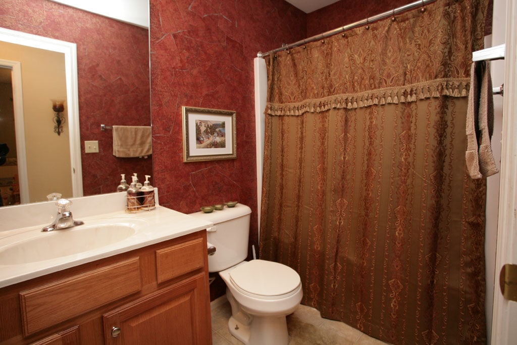 Red wallpaper in bathroom with gold shower curtain.