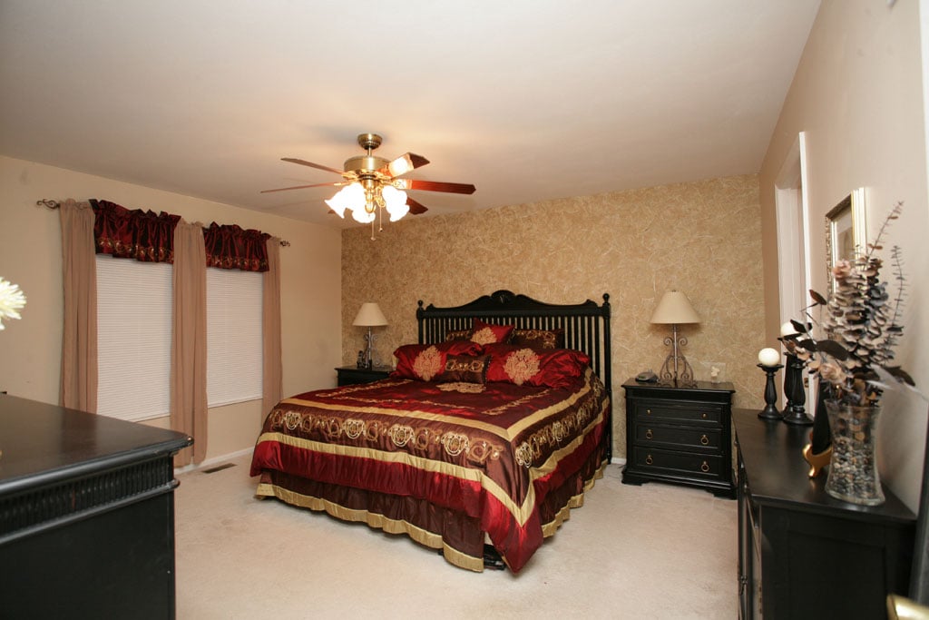 The master suite with wallpaper on the wall at the head of the bed and a ceiling fan.