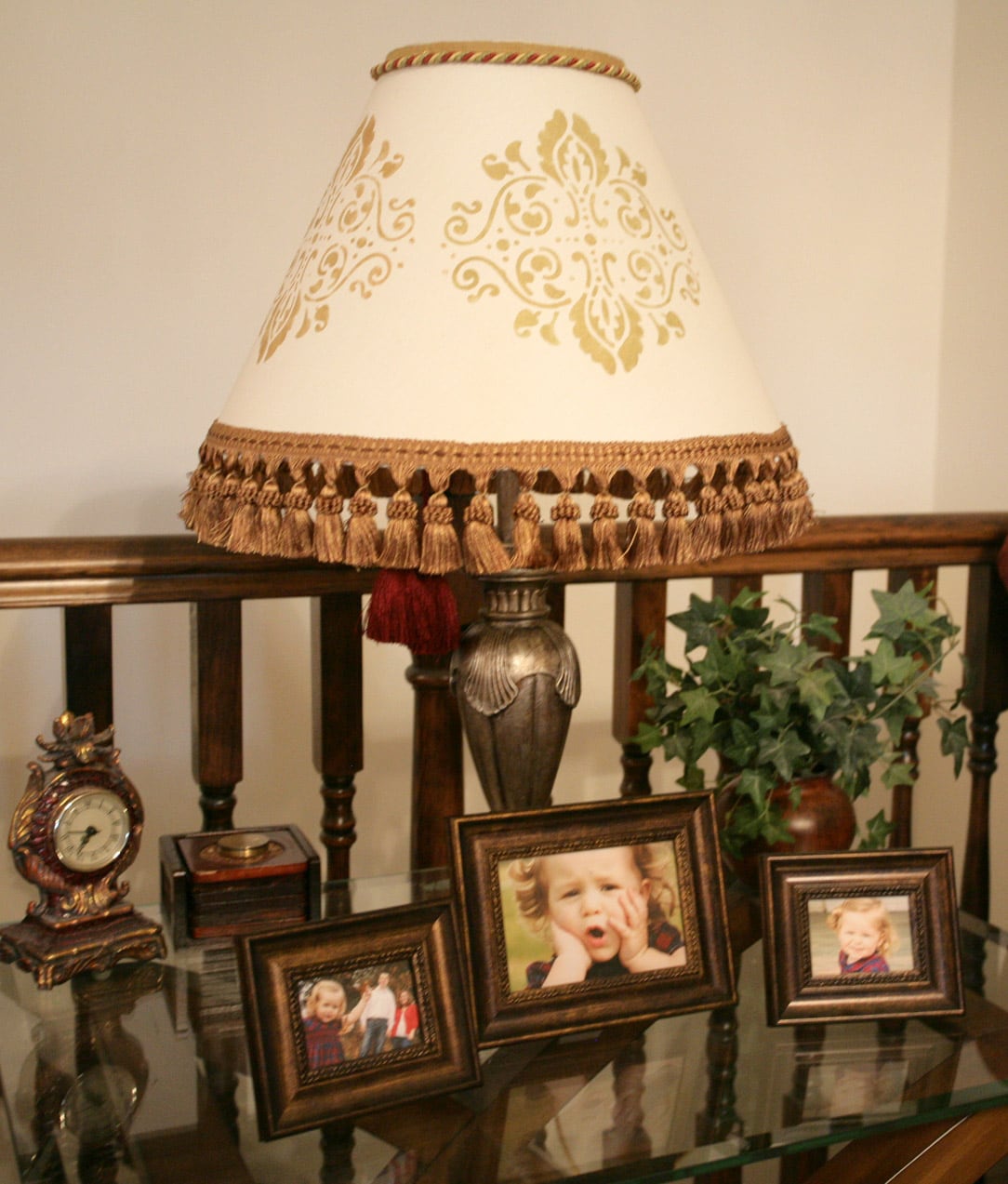 The stencilled lamp on a table with pictures around it.