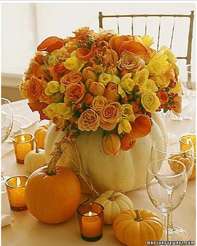 pumpkin filled with yellow, orange, and gold flowers on table.