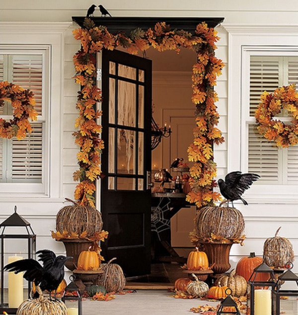 Fall leaves around dark wood door of house.   Black fake crows sitting on twig pumpkins on porch.