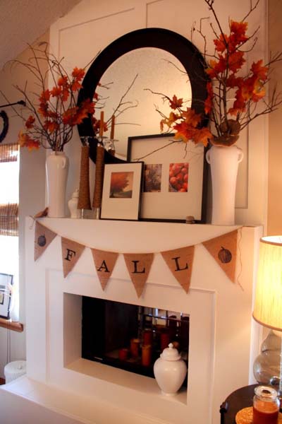 Burlap fall mantel flag on white mantel and large vases of red leaves and a large mirror on the wall.