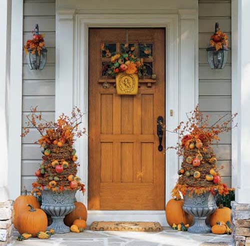 Front door of house with topiaries in ornate outdoor planters and pumpkins around them.