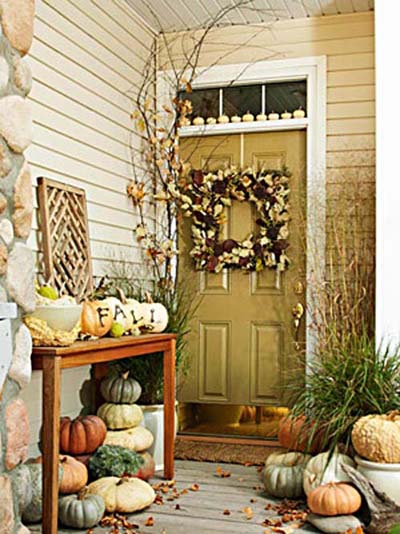 Wreath on pale yellow front door and pumpkins on the porch and outdoor side table.