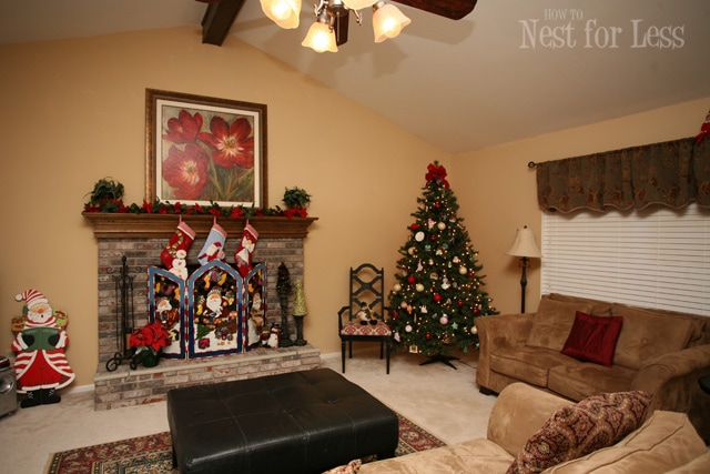 A Christmas tree in the corner, fireplace mantel, and Santa beside the mantel.