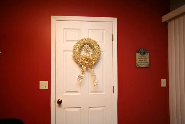 A red wall, white door and a gold wreath.