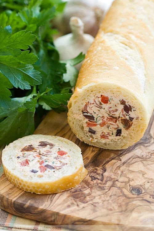 A stuffed baguette bread on a cutting board with a piece already cut.