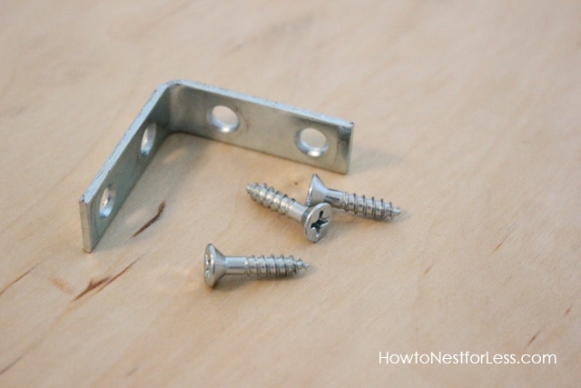 Metal screws and metal bracket on top of plywood.