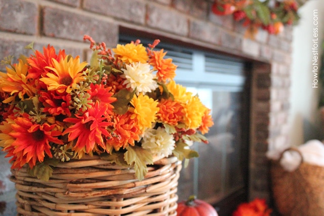 Basket of yellow, red, gold flowers by fireplace.