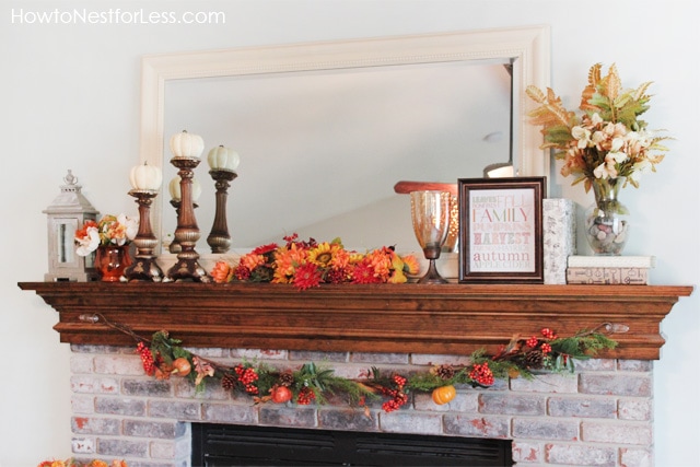 Fireplace mantel with autumn leaves and candle stick holders with pumpkins on them.