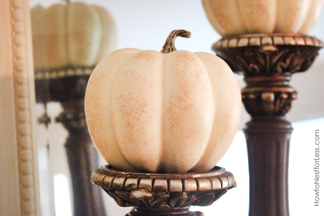 Candlestick holders with white mini pumpkins on top.