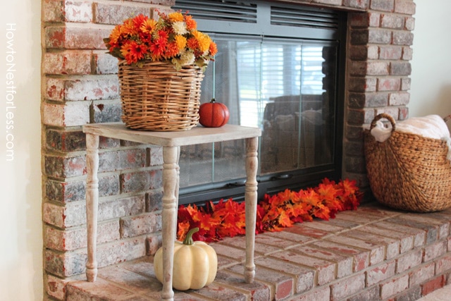 A basket of flowers on a table by the fireplace and red and orange leaves in front of the fireplace.