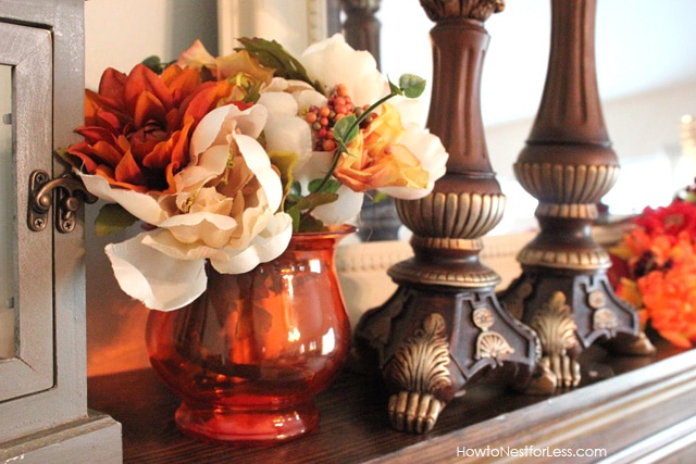 Red vase filled with white and orange flowers on the mantel.