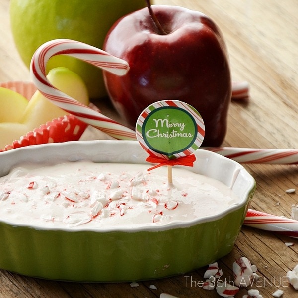 A red apple and a candy cane beside a dip in a green bowl.