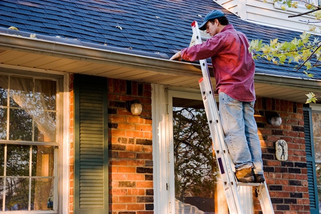 Man on ladder cleaning the gutters.