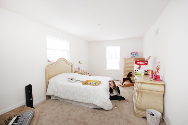 A little girls room with a child sitting on the floor beside the bed.