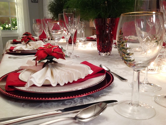 White plates with red chargers and a poinsettia on top of the napkin.