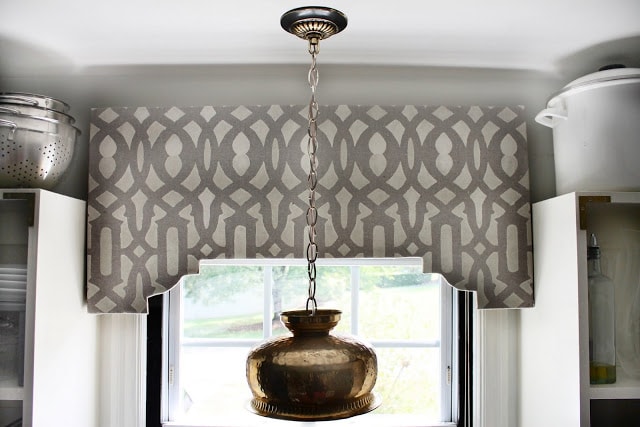 Diy stenciled cornice board with a brass light fixture hanging in front of it.