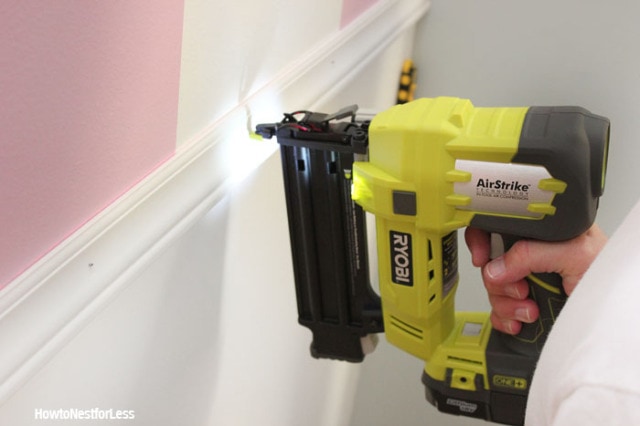 A cordless nail gun is used to secure a piece of chair rail molding to a wall