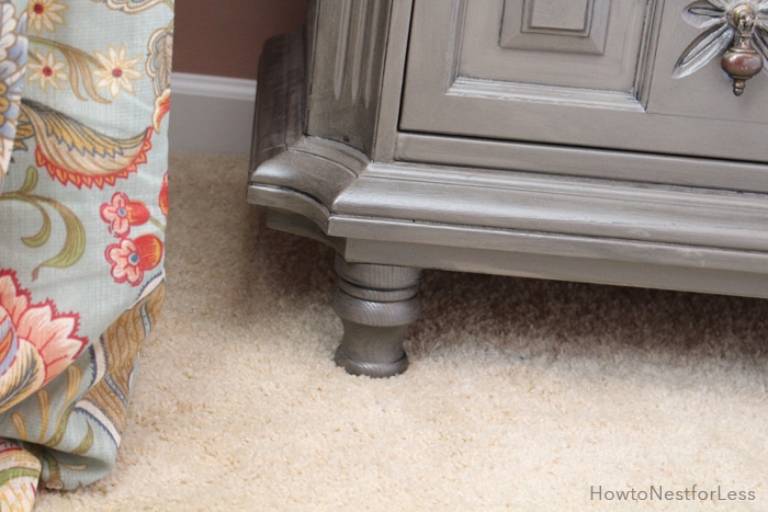 The nightstand on the carpet with legs on it.