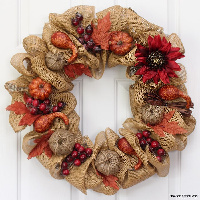 Burlap wreath on a for with flowers and mini pumpkins on it.