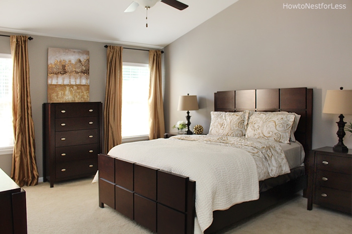 Dark brown bed frame and dresser and white bedding in bedroom.