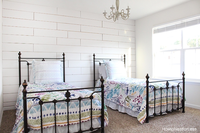 Two wrought iron beds in front of white planked wall.