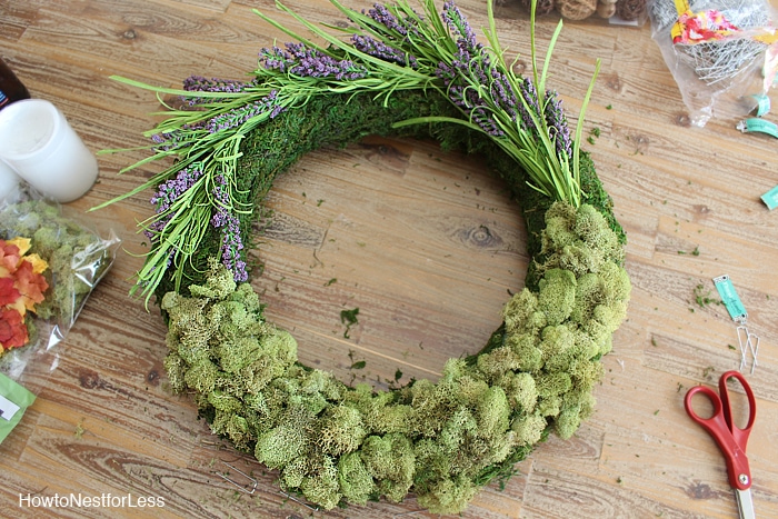 Adding the dried flowers and acorns to the mossy wreath sitting on the desk.