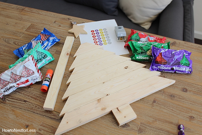 Wooden cut out Christmas tree with packets of Hershey's kisses beside it.