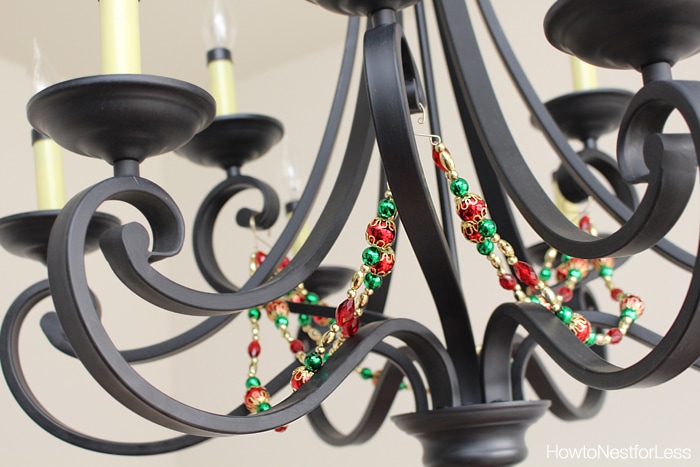 A metal chandelier with red and green and gold string of ornaments around it.