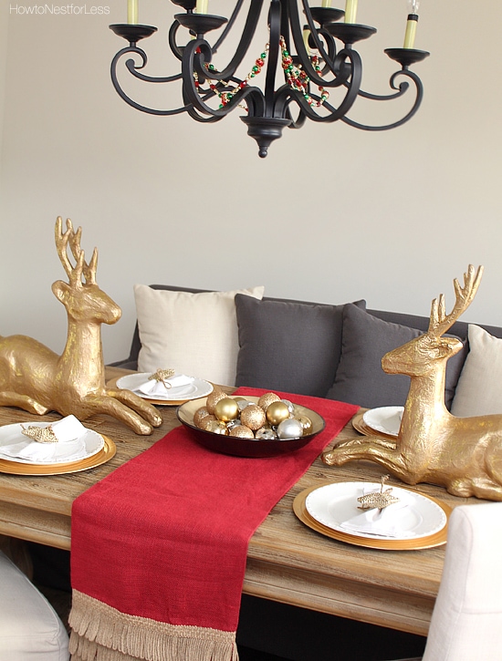Table set for Christmas with two gold deer facing each other and a bowl filled with gold ornaments.