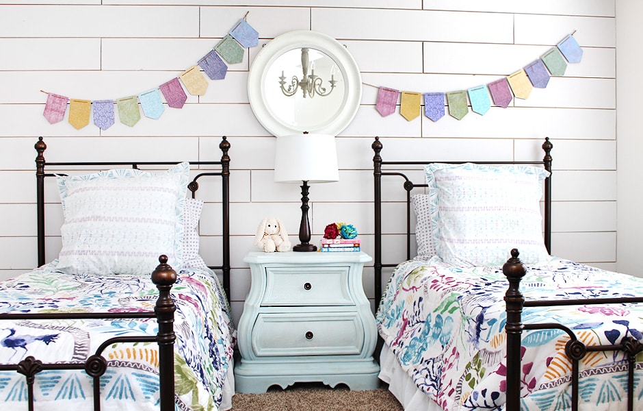 A child's bedroom with shiplap walls and wrought iron beds.