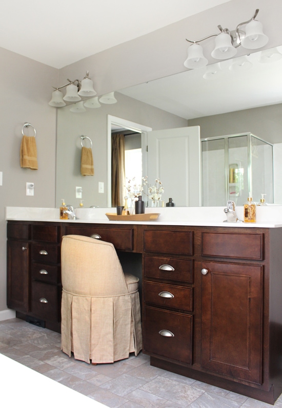 Master bathroom with a dark wood vanity and light colored fabric chair at the vanity.