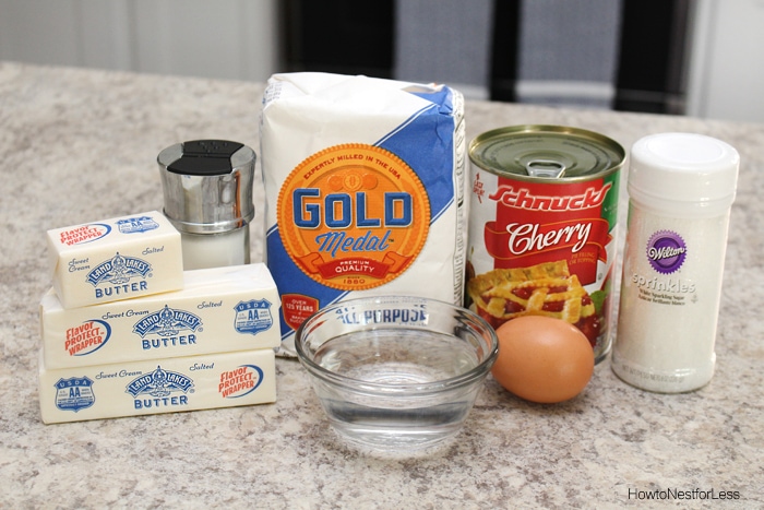 Butter, flour, cherry pie filling, sprinkles, egg and water on the counter for the pies.