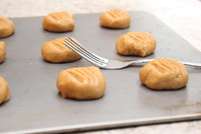 The peanut butter cookie dough on a baking sheet being flattened with a fork.