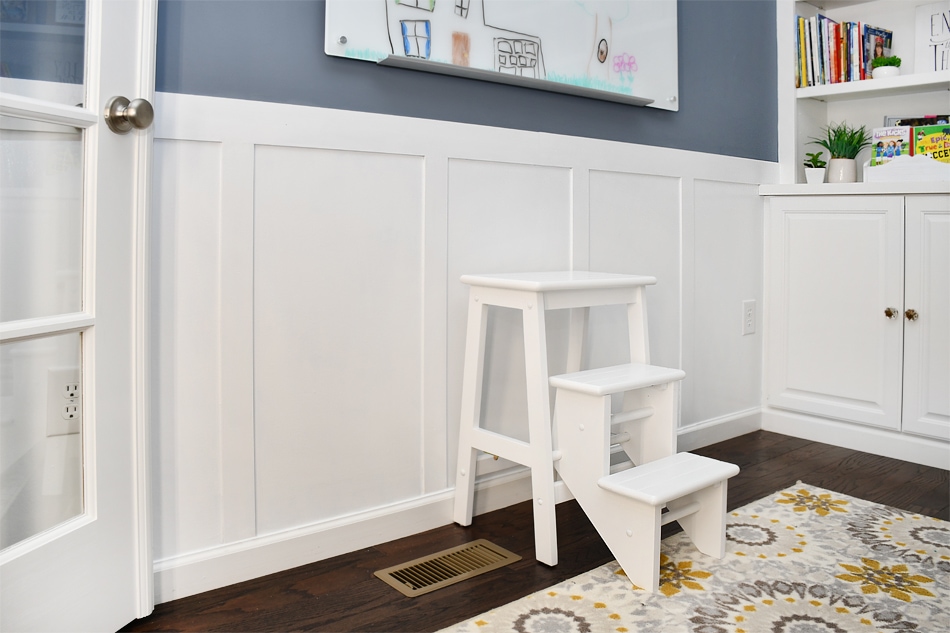 White boards with a gray blue painted wall and a small step stool in front of the boards.