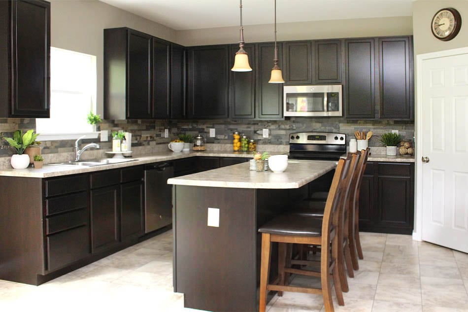 Dark wood island in kitchen with chairs around it.