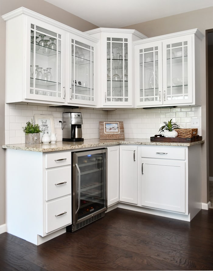 A side cabinet with clear glass and wine glasses inside plus a wine fridge.