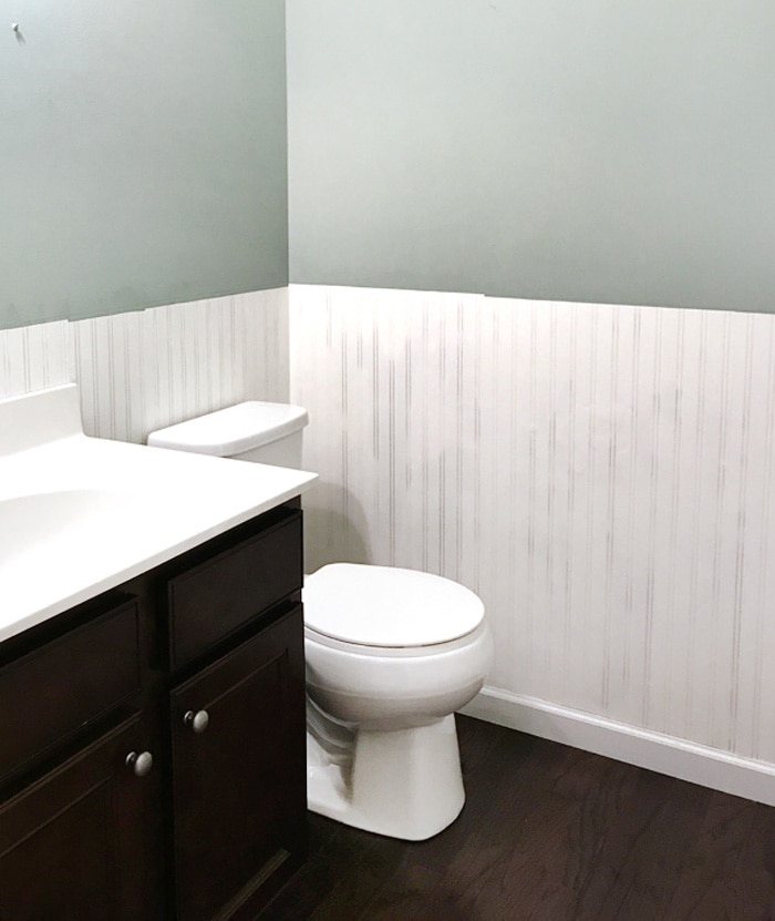 A bathroom with dark wooden floors, a dark cabinet with white counters.