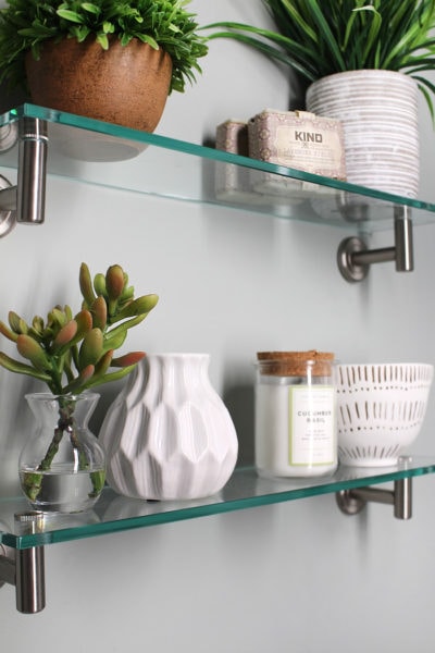 closeup of glass shelves with white vases and bathroom accessories on them