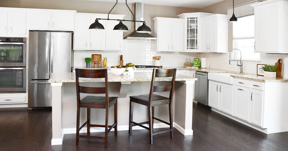 A white kitchen island with two brown wooden chairs at the kitchen island and lights above it.