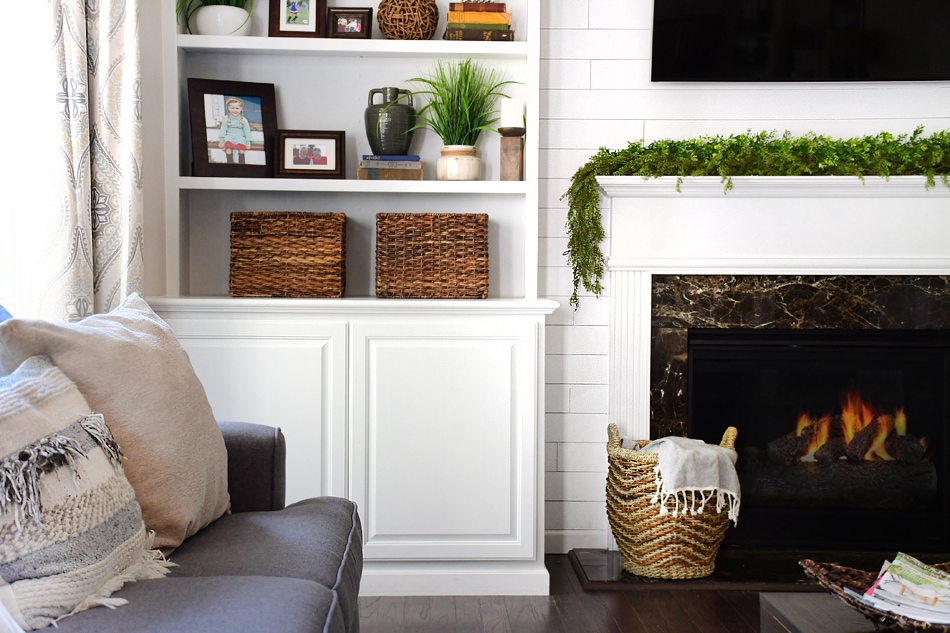 A cozy fireplace, a neutral couch, built in shelves and a shiplap white wall.