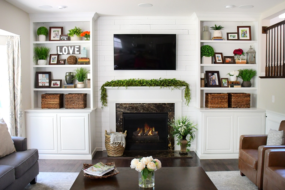 A white neutral living room with a fireplace on and flowers on the coffee table.