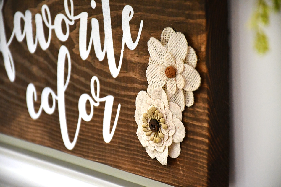 Putting little beige fabric flowers on the wood sign.