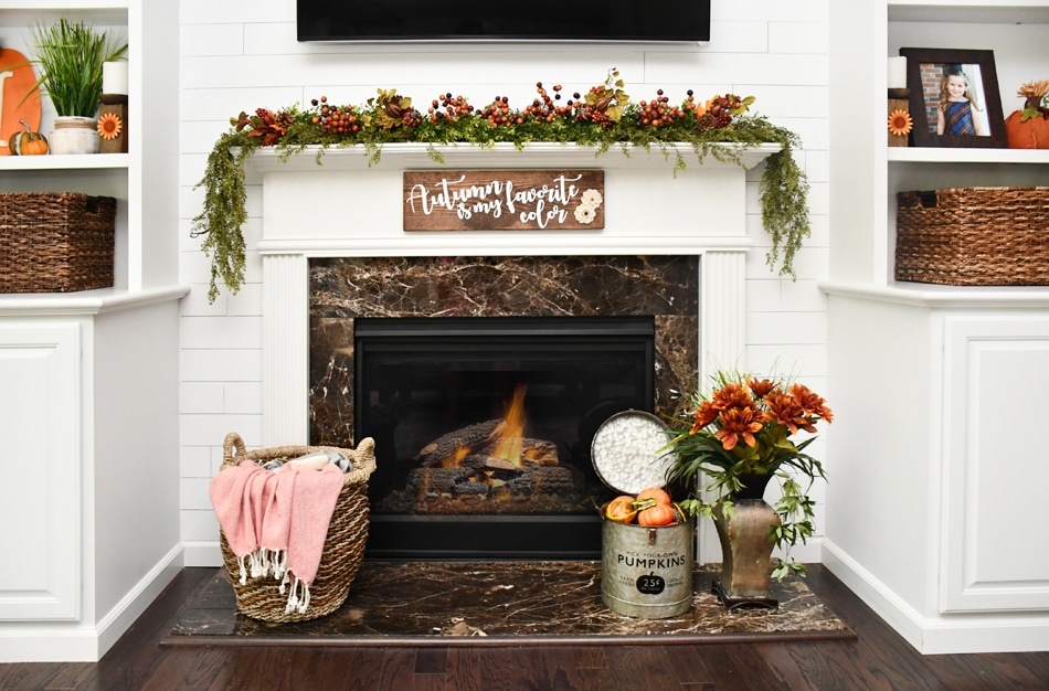 White fireplace mantel with greenery on top and wood diy sign hanging above it.