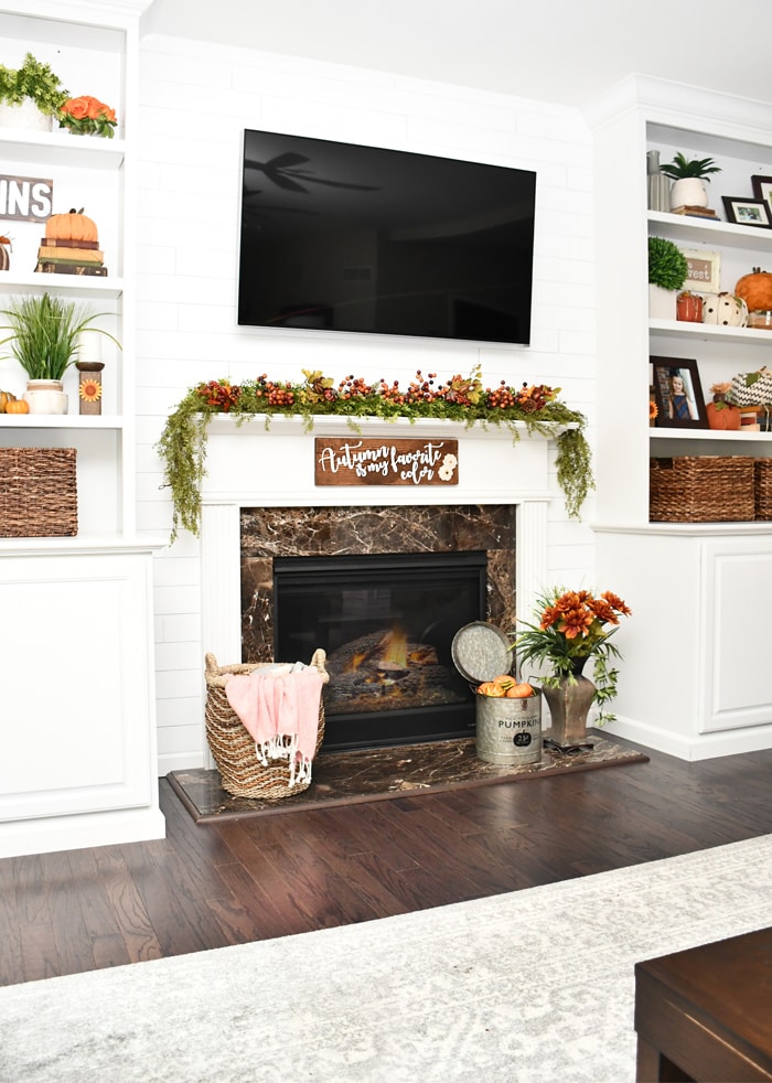 Flowers in large vase in front of fireplace.