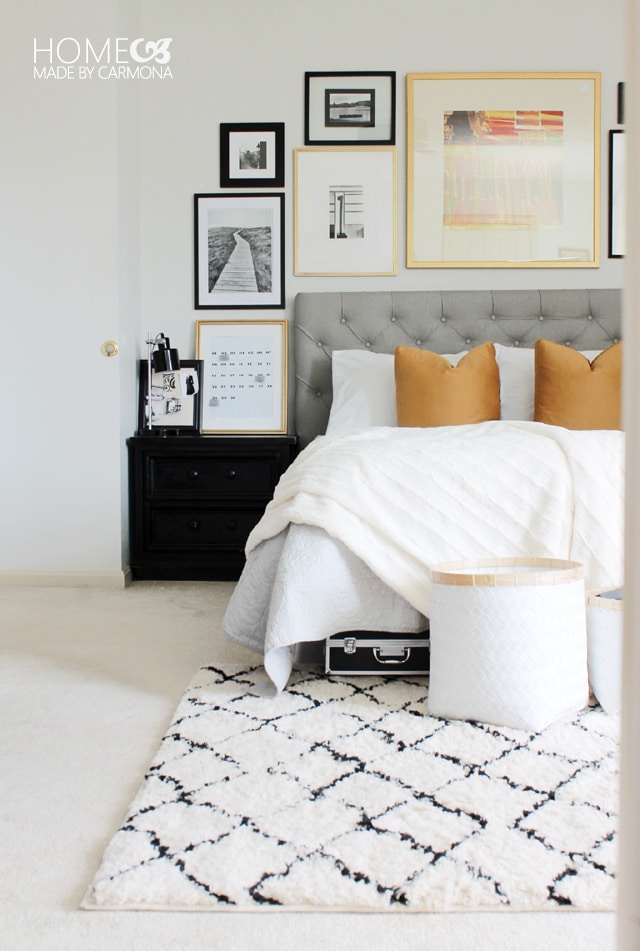 Grey headboard, white and black rug and mustard colored pillows on bed.