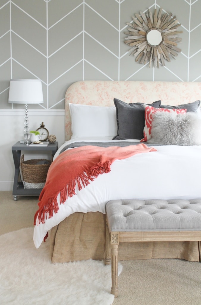 Grey stool and white and grey wallpaper with white bedding and a red throw blanket in master bedroom.