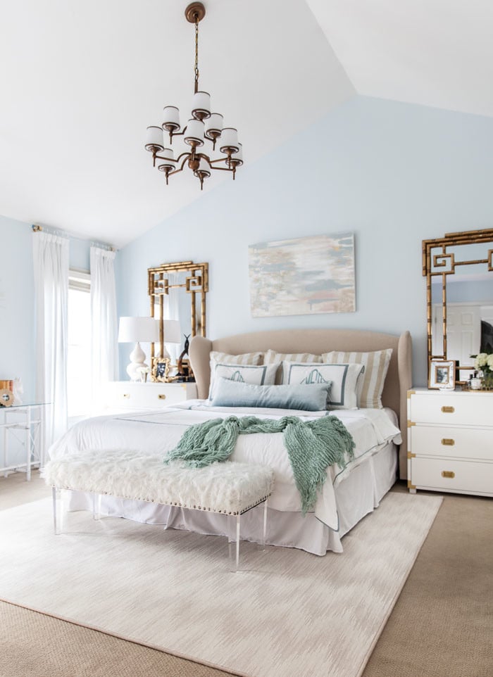 Baby blue walls, white rug, white bedding and green throw blanket on bed in master bedroom.