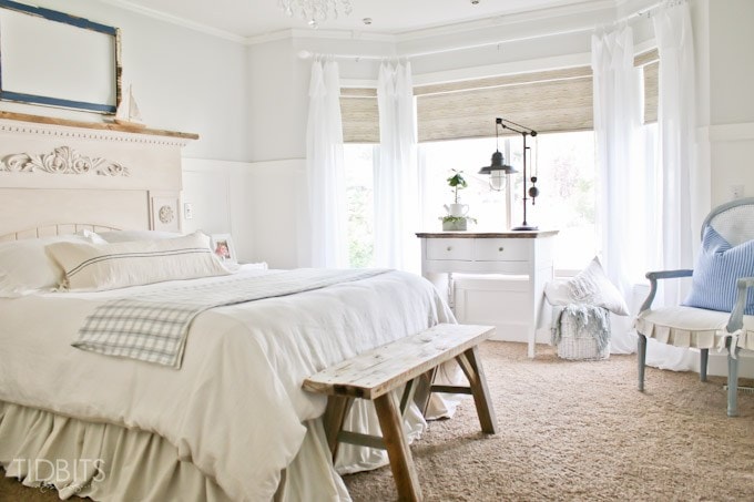 All white bedroom with light blue pillows on chair.